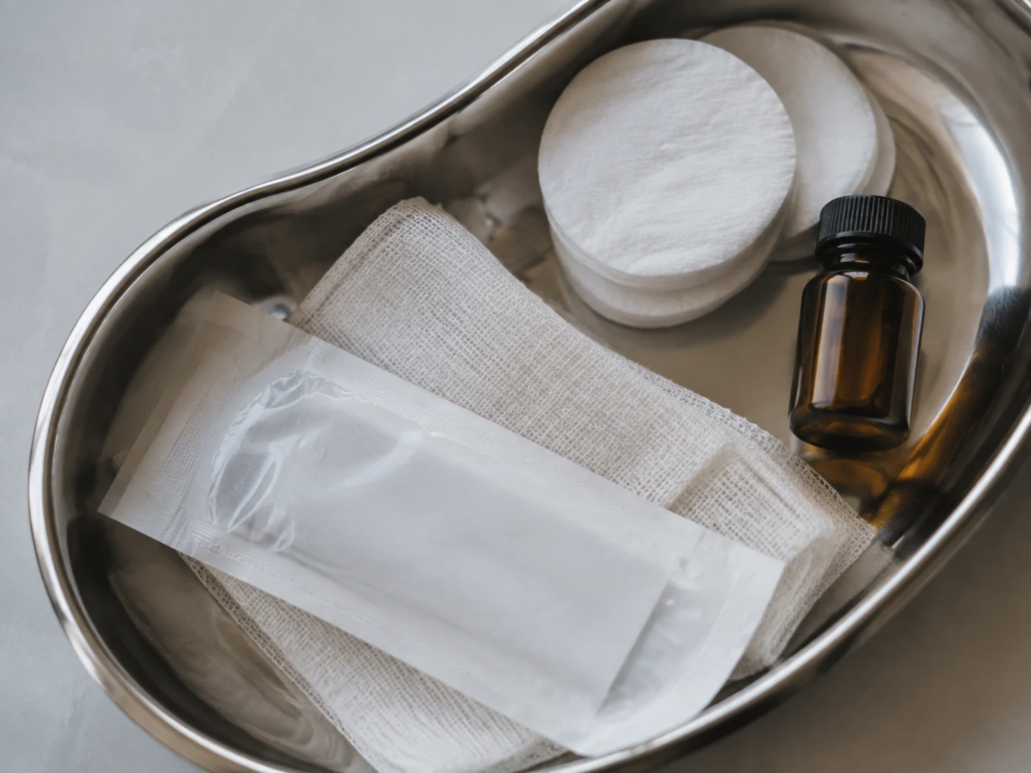 Polished steel tray with cotton rounds, a capped vial and sealed supplies